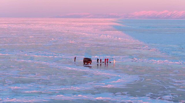 Aerial view of a van and people on the frozen surface of Lake Baikal during sunset in Khuzhir, Irkutsk Oblast, Russia.