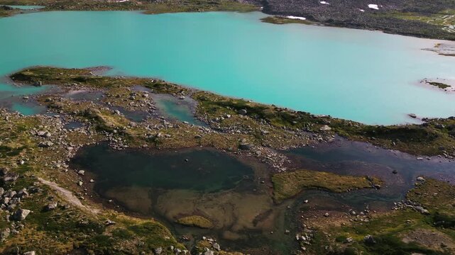 Aerial view of the turquoise glacial lake along the Old Strynefjell Mountain Road with rocky terrain and mossy patches in Stryn Municipality, Vestland, Norway.