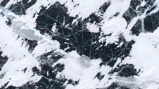 Aerial view of the frozen surface of Lake Baikal featuring intricate white ice patterns and deep blue cracks in Khuzhir, Irkutsk Oblast, Russia.