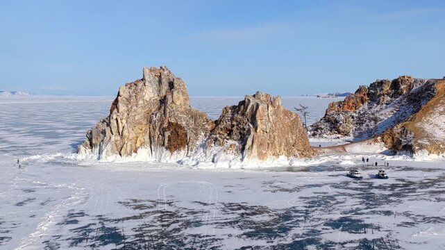 Aerial view of the iconic Shamanka Rock surrounded by the vast frozen expanse of Lake Baikal with hovercraft on the ice in Khuzhir, Irkutsk Oblast, Russia.