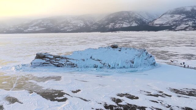 Aerial view of the frozen rocky island on Lake Baikal with snow-covered ice and people walking nearby in Khuzhir, Irkutsk Oblast, Russia.