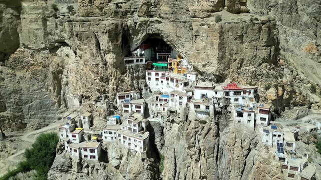 Aerial view of Phukthal Gompa monastery built into a cliffside cave with white buildings and rugged mountain terrain in Phugtal, Himachal Pradesh, India.
