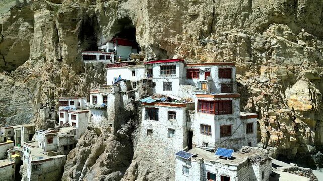 Aerial view of Phukthal Gompa monastery built into a steep rocky cliffside with traditional white walls and red window frames in Phugtal, Himachal Pradesh, India.