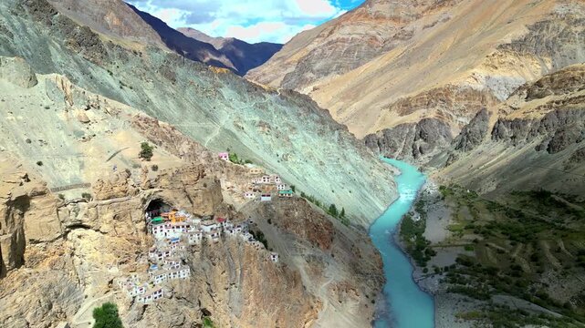 Aerial view of the remote Phukthal Gompa monastery built into a rugged cliffside overlooking the turquoise Lungnak River in Phugtal, Himachal Pradesh, India.