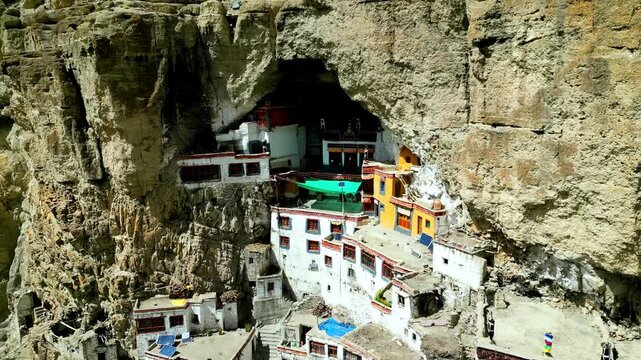 Aerial view of Phukthal Gompa, a historic Buddhist monastery built into a cliffside cave, featuring white and yellow walls and traditional architecture in Phugtal, Himachal Pradesh, India.