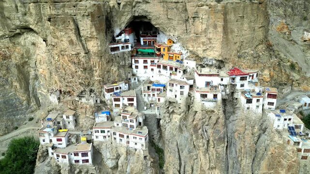 Aerial view of Phukthal Gompa monastery built into the steep cliffside with white buildings and traditional architecture in Phugtal, Himachal Pradesh, India.
