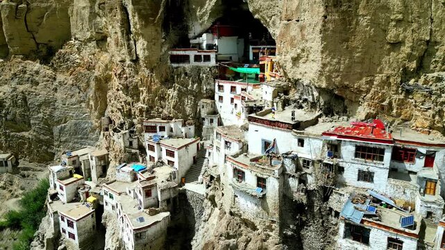 Aerial view of the remote Phukthal Gompa monastery built into a steep cliffside with white buildings and red roofs in Phugtal, Himachal Pradesh, India.