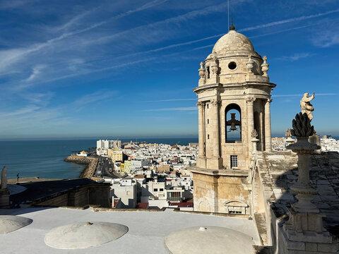 View of the historic bell tower of the Cathedral of Cadiz overlooking the white buildings of the city and the Atlantic Ocean under a clear blue sky in Cadiz, Andalusia, Spain.