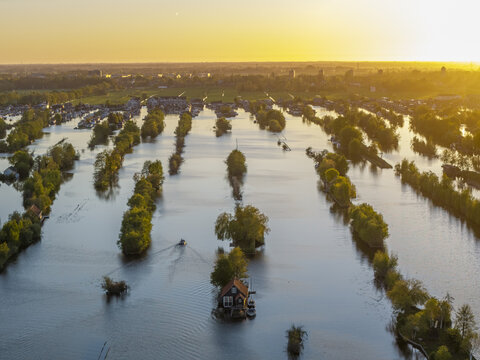 Aerial view of Scheendijk featuring small islands with lush trees and houses surrounded by calm water during golden hour in Breukelen, Utrecht, Netherlands.