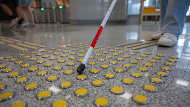 A blind woman walks on tactile paving. Close-up of her feet and a walking stick.