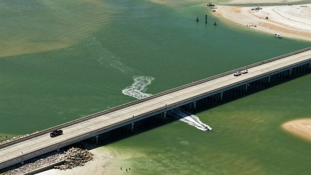 Aerial view of Matanzas Inlet bridge with vehicles crossing over the water and a boat navigating the channel near the sandy shores of St. Johns County, Florida, United States.