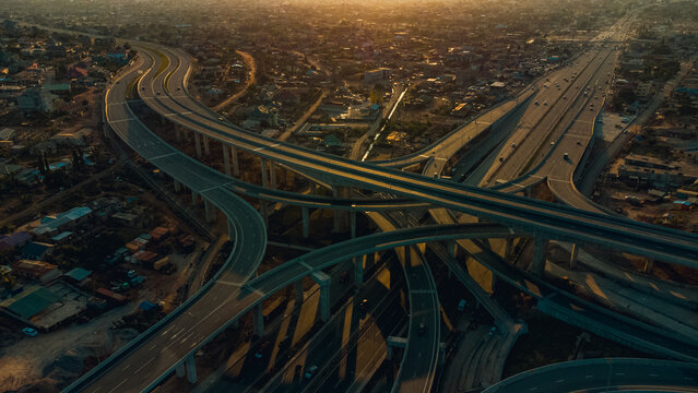 Aerial view of the multi-level Pokuase Interchange featuring sweeping concrete ramps and highway lanes under warm golden hour light, Ga North Municipal, Greater Accra Region, Ghana.