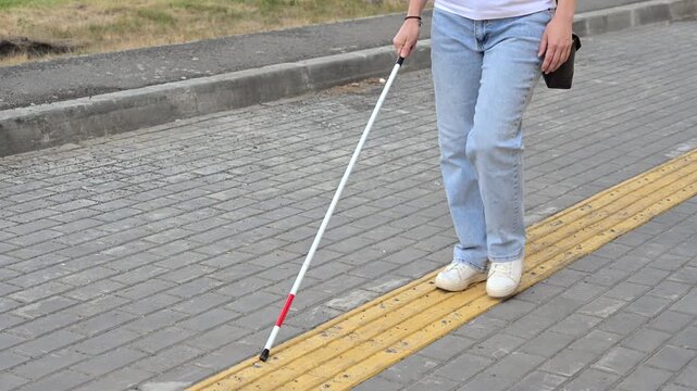 A blind woman walks on tactile paving. Close-up of her feet and a walking stick.