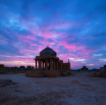 View of a historic tomb at Makli Graveyard under a vibrant purple and blue sunset sky in Thatta, Sindh, Pakistan.