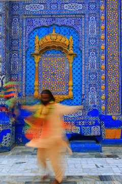 View of a devotee spinning in a traditional dance at the Dargah Sachal Sarmast, featuring intricate blue tile work and golden architectural details in Ranipur, Sindh, Pakistan.