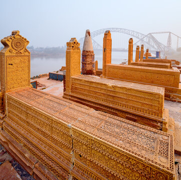 View of the intricately carved historic graves at the Seven Sisters site, with the Lansdowne Bridge visible in the background in Sukkur, Sindh, Pakistan.