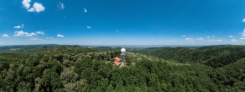 Aerial view of the radar station on Fruska Gora surrounded by dense green forests under a clear blue sky in Serbia.