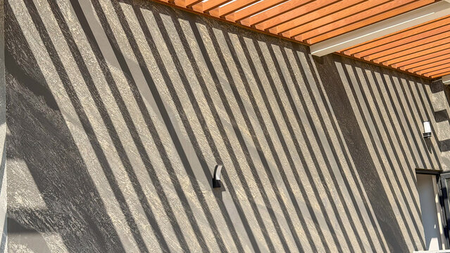 Abstract architectural shadows from a wooden pergola creating striking diagonal lines on a textured modern wall. Minimal geometric background with sunlight, pattern and copy space for contemporary 