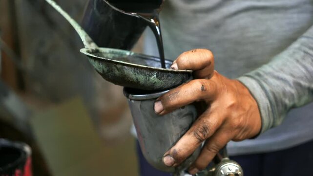 Pouring Paint into Spray Gun Cup 
An industrial worker pours liquid black paint through a mesh strainer into a spray gun cup inside a workshop, and highlighting preparation processes 