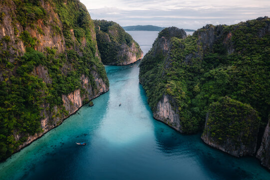 Aerial view of Pi Leh Bay featuring limestone cliffs, lush vegetation, and clear turquoise water with traditional long-tail boats in Tambon Ao Nang, Chang Wat Krabi, Thailand.