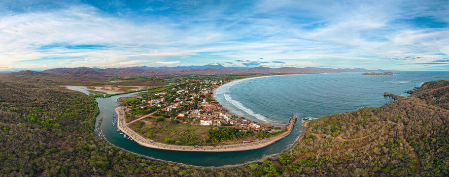 Aerial view of Playa Punta Perula showing the coastal town, the curved beach, the river meeting the sea, and the surrounding lush landscape in Perula, Jalisco, Mexico.