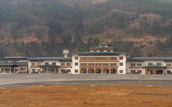 View of Paro International Airport terminal building with traditional Bhutanese architecture and intricate woodwork, set against forested mountains in Paro, Paro, Bhutan.