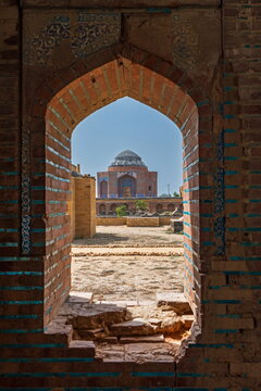 View of the historic Makli Necropolis seen through an ancient brick arched doorway with intricate blue tile details in Thatta, Sindh, Pakistan.