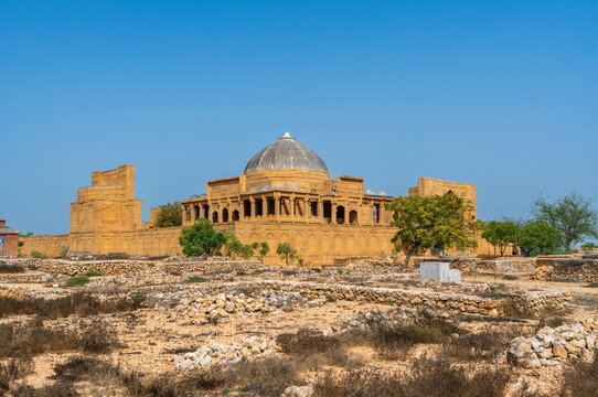 View of the historic Makli Necropolis mausoleum with its stone dome and arched architecture set against a clear blue sky in Thatta, Sindh, Pakistan.