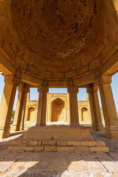 View of the historic sandstone mausoleum at Makli Necropolis featuring intricate stone carvings, a domed roof, and arched entrances in Thatta, Sindh, Pakistan.