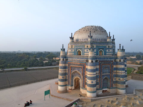 Aerial view of the historic blue-tiled tomb with intricate architectural patterns, surrounding landscape, and people sitting on the ground in Uch Sharif, Punjab, Pakistan.