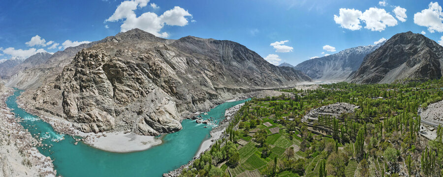 Aerial view of the Gol Valley with the turquoise Indus River flowing through lush green fields and rocky mountains in Skardu, Gilgit Baltistan, Pakistan.
