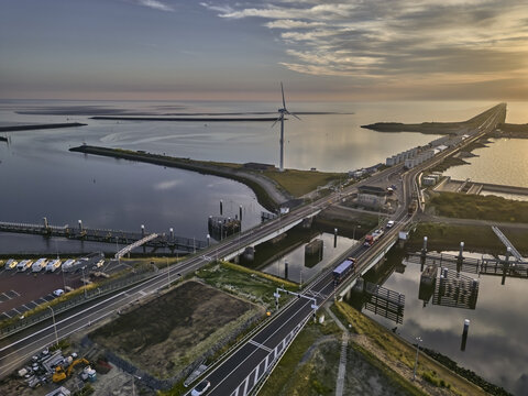 Den Oever, Netherlands - 19 June 2026: Aerial view of the Stevinsluizen sluice dams and A7 highway swing bridges with a wind turbine and the Waddenzee in early morning light.