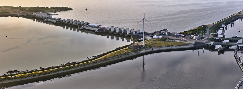 Den Oever, Netherlands - 19 June 2026: Aerial view of Stevinsluizen with sluice dams, swing bridges, and a wind turbine in early morning light.