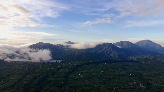 Aerial view of the lush green mountains and rolling hills of Wanagiri with low-hanging clouds and a serene landscape in Sukasada, Bali, Indonesia.