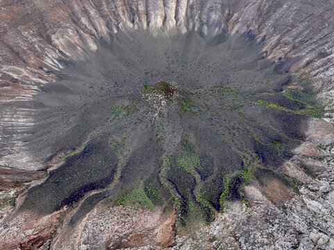 Aerial view of a volcanic crater with dark lava flows and sparse green vegetation in Lanzarote.