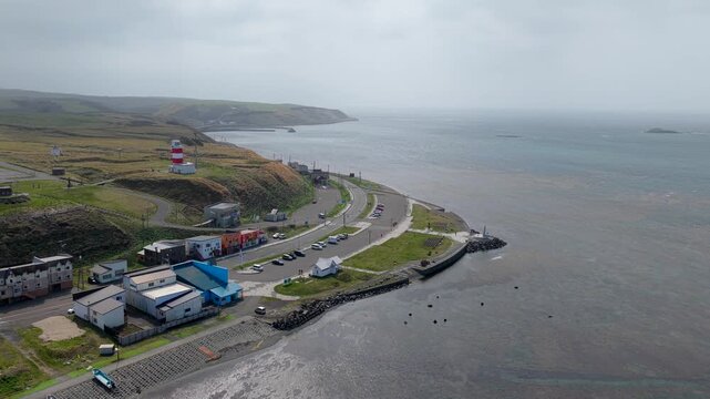 Aerial view of Cape Soya lighthouse, coastal road, and buildings along the rugged shoreline in Wakkanai, Hokkaido, Japan.