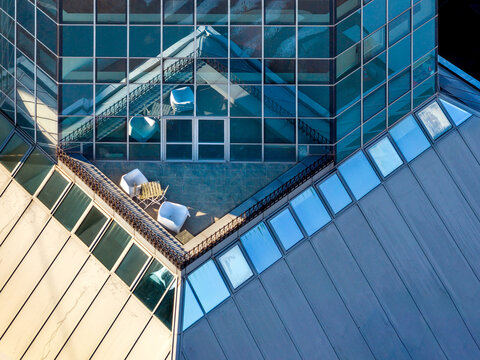 Aerial view of a modern building rooftop terrace with white chairs and a small table, featuring glass facades and metal roofing in Belgrade, City of Belgrade, Serbia.