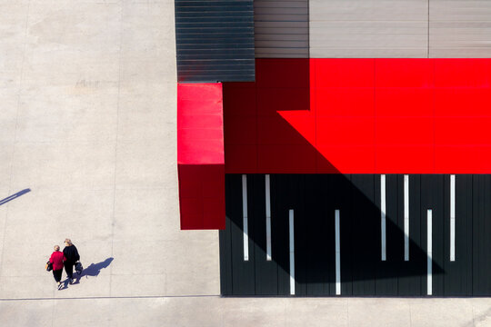 Aerial view of two people walking on a concrete plaza beside a modern building with striking red and black geometric panels in Belgrade, City of Belgrade, Serbia.