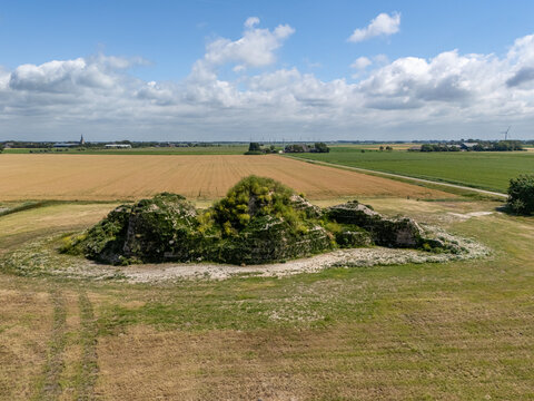 Aerial view of the historic Dijk van een wijf mound covered in lush green vegetation, situated amidst expansive agricultural fields under a bright blue sky in Oosterbierum, Friesland, Netherlands.