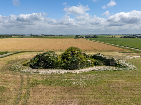 Aerial view of the historic Dijk van een wijf mound surrounded by vast agricultural fields and green meadows under a blue sky in Oosterbierum, Friesland, Netherlands.