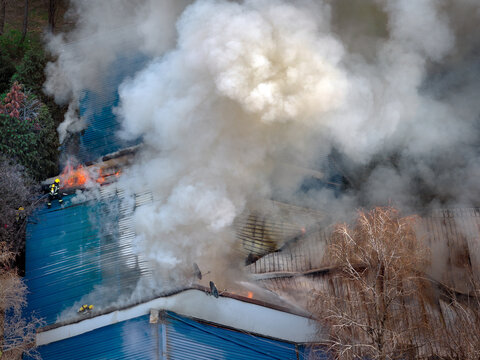 Aerial view of a building fire with thick smoke billowing from a blue roof as a firefighter works to extinguish the flames in Belgrade, City of Belgrade, Serbia.