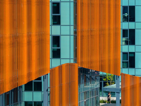 Aerial view of modern building facade with vibrant orange vertical louvers and teal glass panels, featuring a person walking on the ground level in Belgrade, City of Belgrade, Serbia.