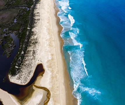 Aerial view of Bettys Beach with turquoise ocean waves, sandy shoreline, and dark coastal inlet in Albany, WA, Australia.