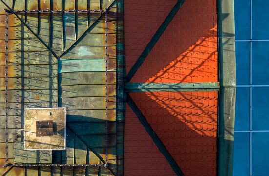 Aerial view of a roof featuring weathered copper sheeting and vibrant red tiles, with a chimney and intricate shadows cast across the surface in Belgrade, City of Belgrade, Serbia.