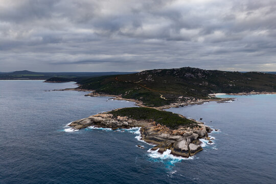 Aerial view of Bettys Beach featuring rugged rocky outcrops, crashing waves, and lush coastal vegetation under a dramatic cloudy sky in Albany, WA, Australia.