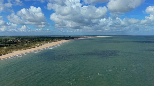 Aerial view video clip of expansive sandy beach, coastal sand dunes, North Sea ocean waves, and blue sky with cumulus clouds in Domburg, Zeeland, Netherlands on a sunny day
