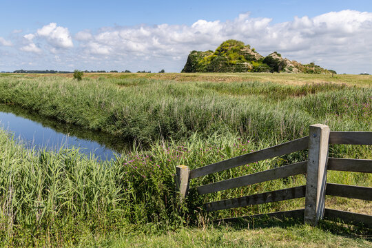 View of the Dijk van een wijf sculpture situated in the green landscape with a canal and wooden fence in Oosterbierum, Friesland, Netherlands.