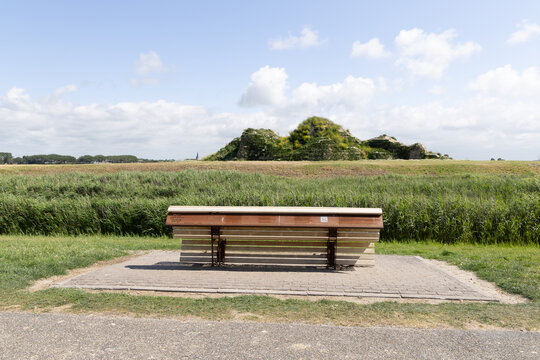 View of the Dijk van een wijf bench situated in a grassy landscape with a small hill in the background under a blue sky in Oosterbierum, Friesland, Netherlands.
