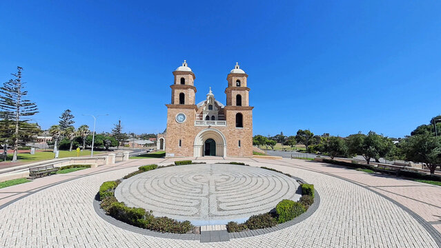 View of St Francis Xavier's Cathedral with its distinctive twin towers and stone facade, set behind a circular stone labyrinth in Geraldton, Western Australia, Australia.