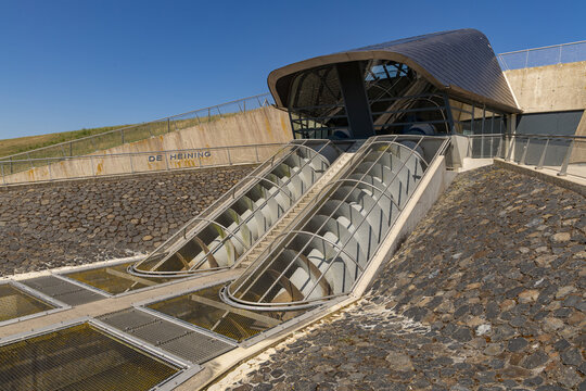 View of the De Heining Archimedes screw pump set into a stone embankment with metal grates and a modern roof structure in Marrum, Friesland, Netherlands.